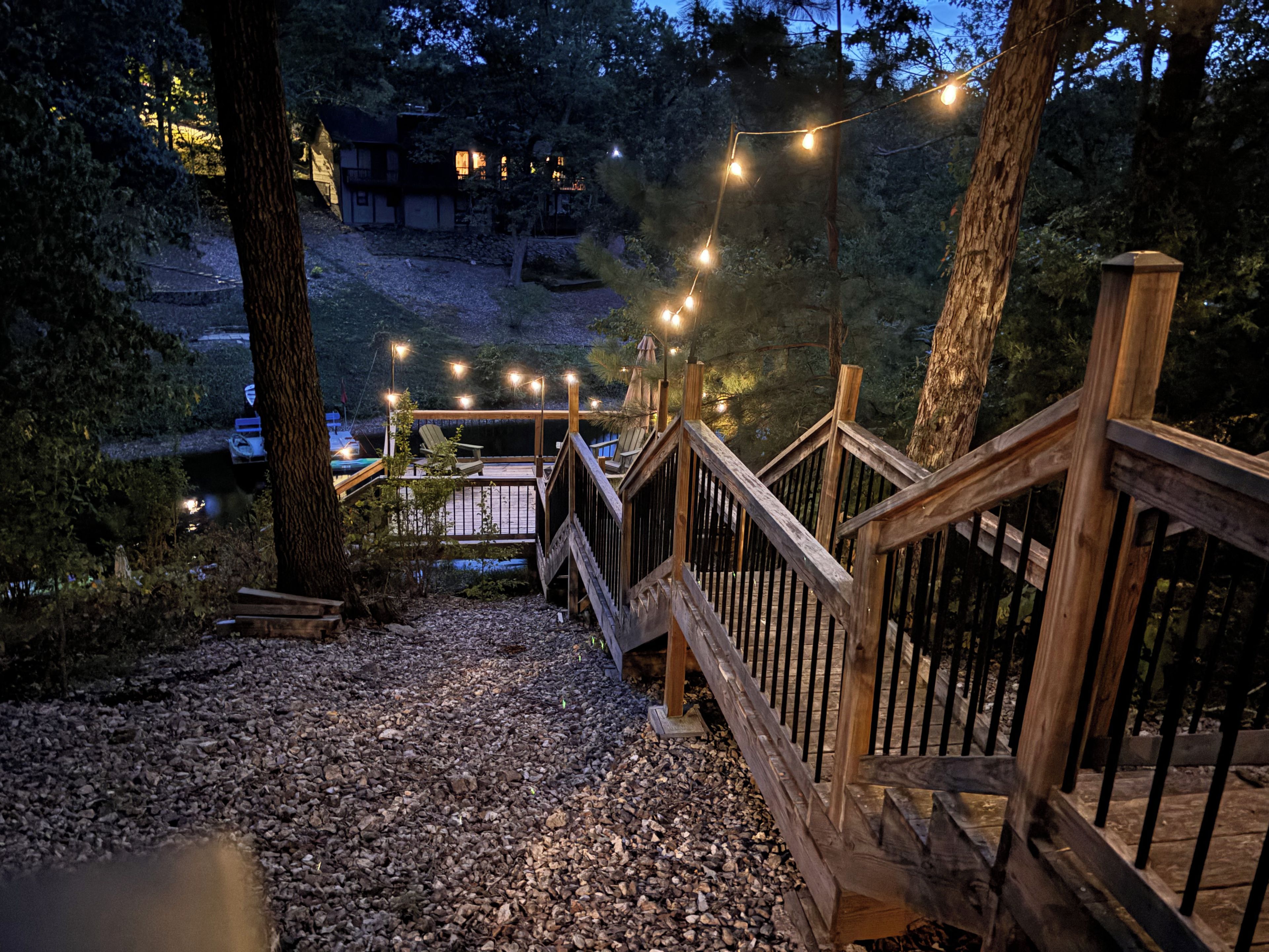 Une terrasse en bois, dotée d’une rambarde, qui mène à un bâtiment, le tout étant entouré d’arbres et de gravier.