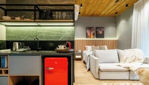A compact living space with a kitchenette, a red refrigerator, a sofa, and a bed.