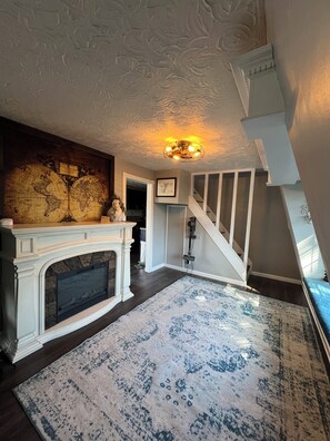Ein Zimmer mit Kamin, einem großen Teppich, einer Treppe und einer Weltkarte an der Wand.
