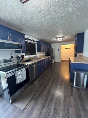 A modern kitchen with stainless steel appliances, blue cabinetry, and a patterned ceiling.