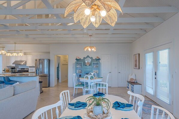 A spacious kitchen with modern appliances, a dining area with white chairs, and a ceiling with exposed beams. - Luxe 4BD Beach House | Sleeps 10 | Beach Access (Galveston)