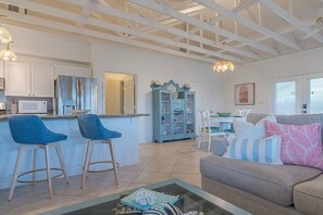 A spacious living area with a kitchen, a dining table, and a sofa with cushions. - Luxe 4BD Beach House | Sleeps 10 | Beach Access (Galveston)