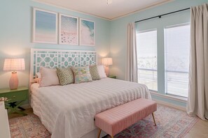 A bedroom with a bed, bedside lamps, a bench, a window with curtains, and wall art. - Luxe 4BD Beach House | Sleeps 10 | Beach Access (Galveston)