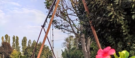 A swing set with a tire swing, surrounded by greenery and flowering plants.