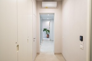 A hallway with a door on the left, a potted plant in the center, and a wall-mounted device on the right. - Loggiato Verga 18th Cent   Suite Carrara Bed&Bros (SIRACUSA)