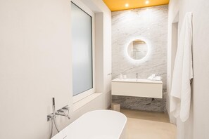 A modern bathroom with a freestanding bathtub, a round mirror, and a built-in sink. - Loggiato Verga 18th Cent   Suite Carrara Bed&Bros (SIRACUSA)