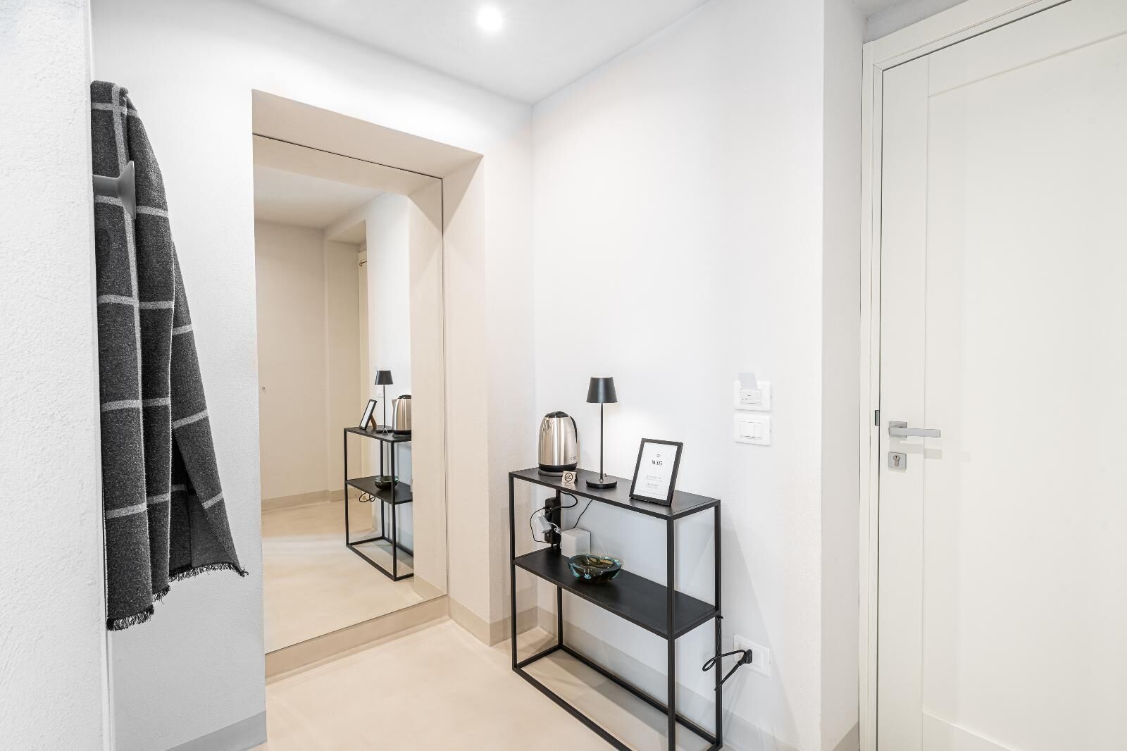A hallway with a mirror, a black console table with a lamp, and a door.