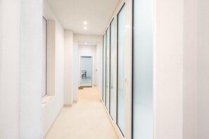 A corridor with a light-colored floor, white walls, and a door at the end leading to a room with a desk and chair. - Loggiato Verga 18th Cent   Suite Carrara Bed&Bros (SIRACUSA)