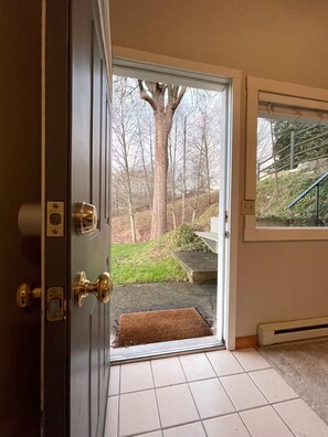 A door leading to a covered outdoor area with a view of a tree and a stone wall. - Private studio in Kenmore perfect for your relaxing getaway (Kenmore)