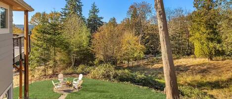 A residential property with a well-maintained lawn, outdoor seating area, and a view of a forested area.