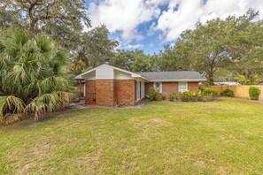 A single-story brick house with a front porch, surrounded by a well-maintained lawn and various trees. - Tabby and Teal Cottage SSI (St. Simons Island)