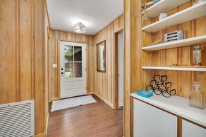 A hallway with wooden walls, a white door with a glass panel, a white radiator, and a white console table with decorative items. - Tabby and Teal Cottage SSI (St. Simons Island)