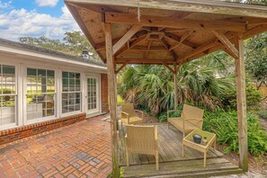 A covered patio with wicker furniture and a brick floor. - Tabby and Teal Cottage SSI (St. Simons Island)