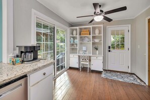A kitchen with a coffee maker, a white chair, and a ceiling fan. - Tabby and Teal Cottage SSI (St. Simons Island)