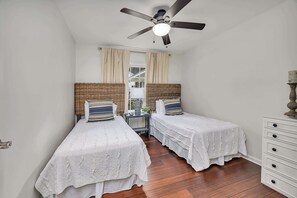 Ein Schlafzimmer mit zwei Einzelbetten, einem Deckenventilator, einem Fenster mit Vorhängen und einem Holzboden.