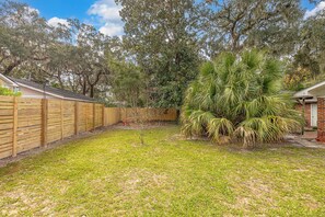 A backyard with a wooden fence, a palm tree, and a grassy lawn. - Tabby and Teal Cottage SSI (St. Simons Island)