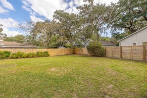 A backyard with a wooden fence, a grassy lawn, and trees. - Tabby and Teal Cottage SSI (St. Simons Island)