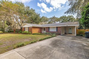 A single-story house with a front garage, a lawn, and mature trees. - Tabby and Teal Cottage SSI (St. Simons Island)