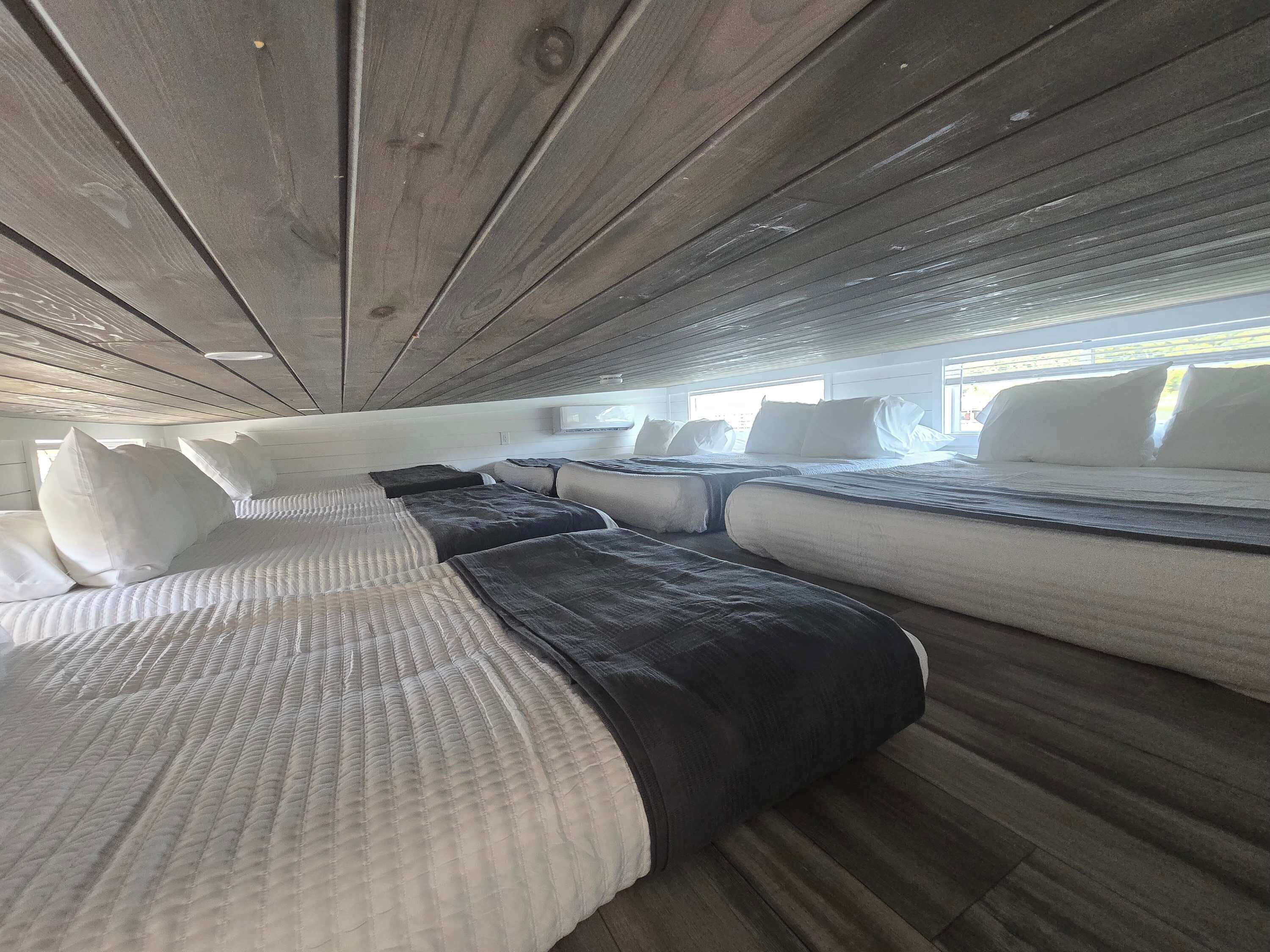 Une cabine avec plusieurs lits disposés en rangée, un plafond en bois et une fenêtre laissant entrer la lumière naturelle.