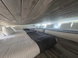 Une cabine avec plusieurs lits disposés en rangée, un plafond en bois et une fenêtre laissant entrer la lumière naturelle.
