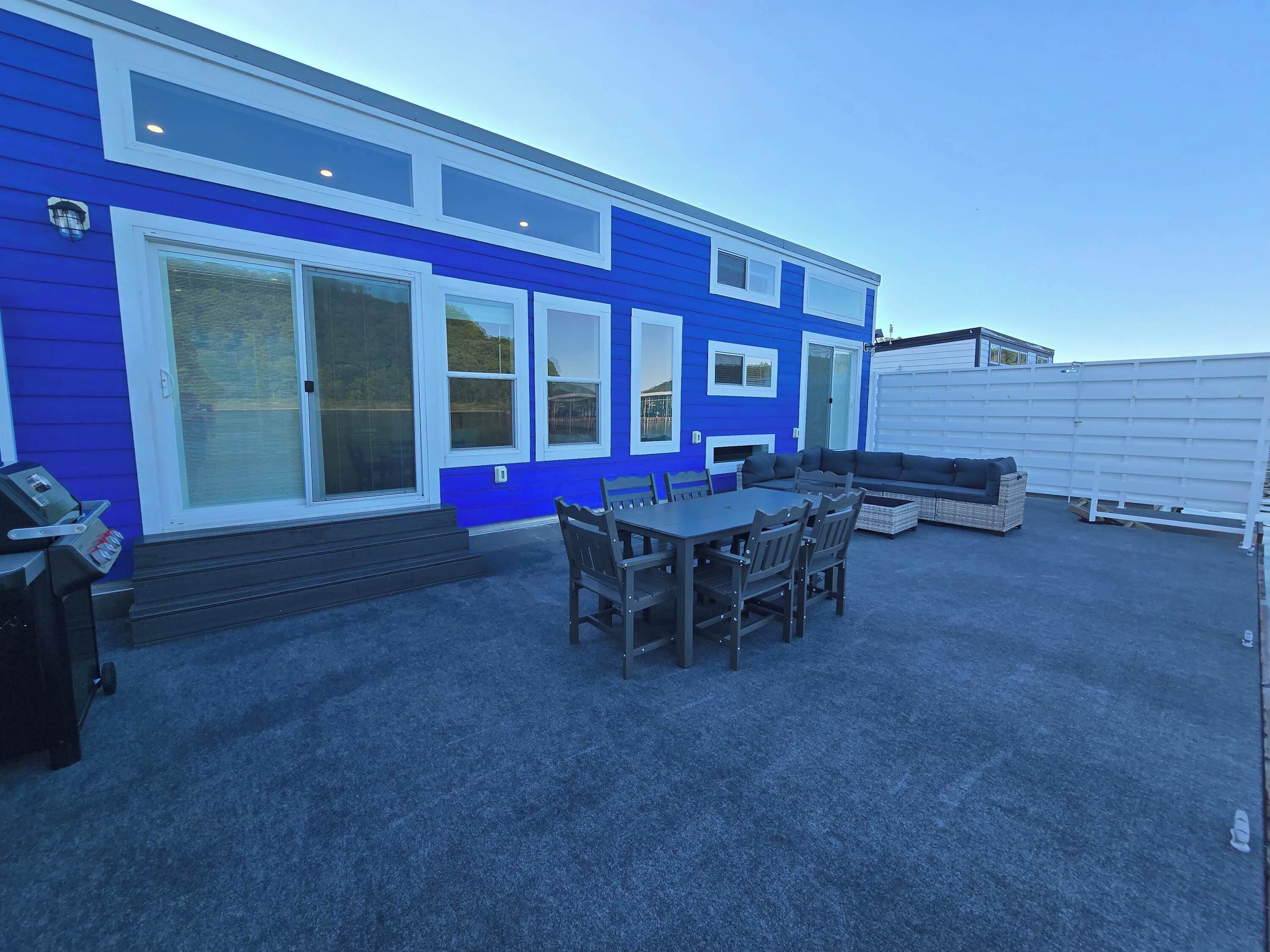 A blue building with a patio area featuring a table and chairs, a sofa, and a grill.