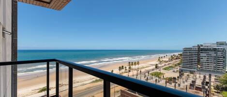 Un balcon offrant une vue sur la plage, l’océan et les bâtiments avoisinants.