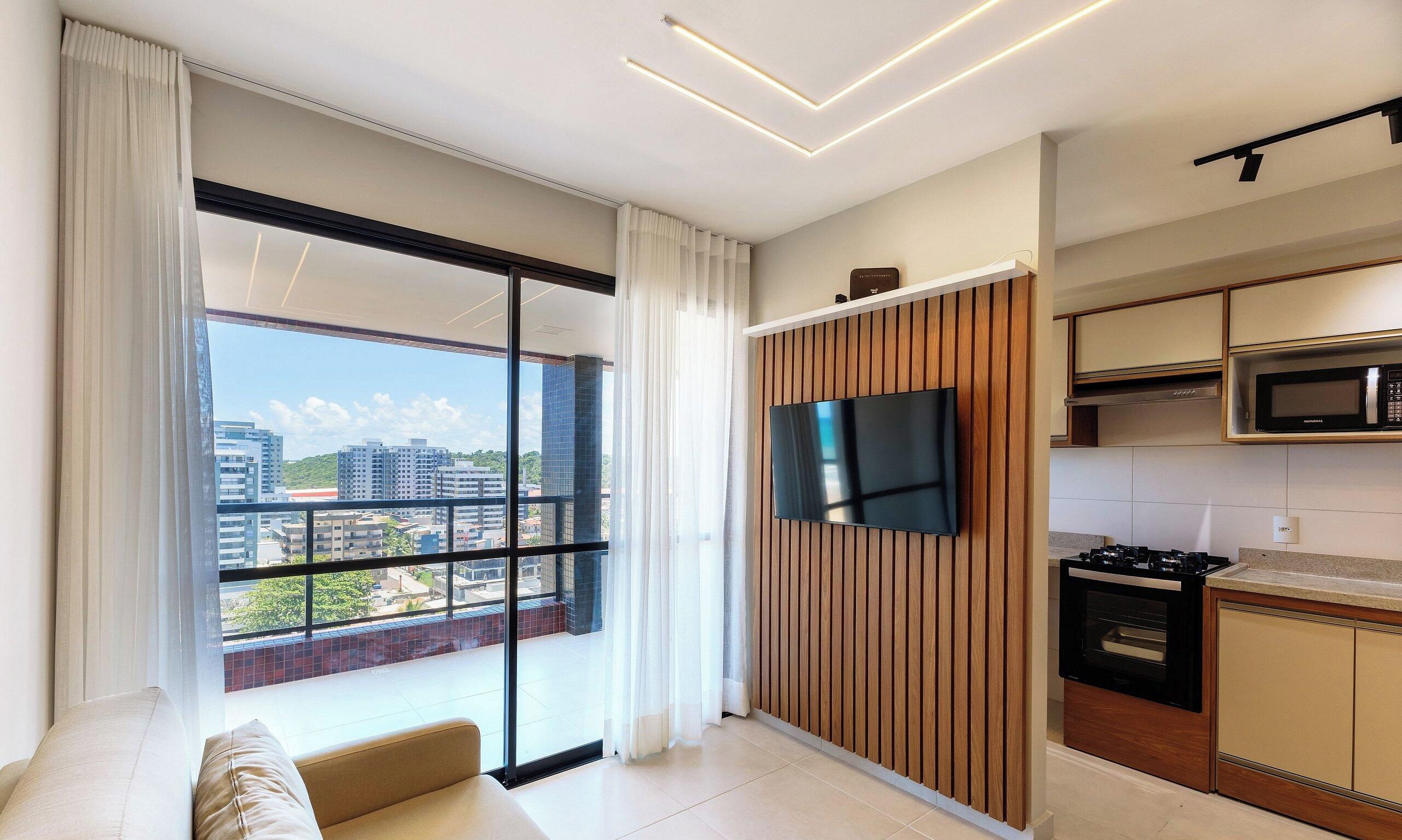 A modern apartment with a balcony, a flat-screen TV, and a kitchen area.