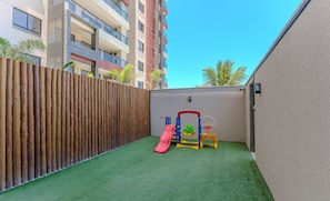 Area giochi esterna recintata con scivolo e altalene.