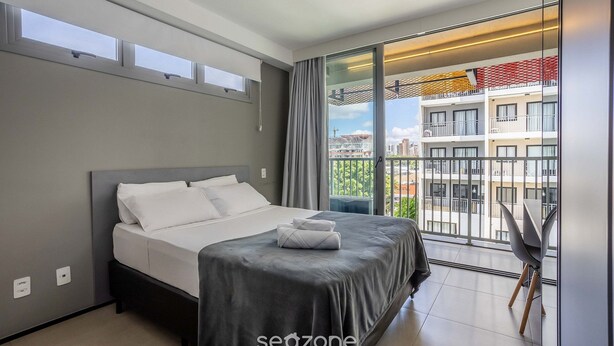 Ein modernes Hotelzimmer mit einem großen Bett, einem Balkon mit Blick auf die Stadt und einem Essbereich mit Tisch und Stühlen.