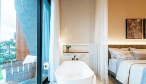 A modern bathroom with a freestanding bathtub, a shower area, and a bed with a headboard.