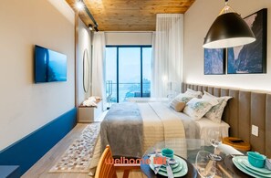 Une chambre d’hôtel moderne dotée d’un grand lit, d’une table à manger avec vue et d’un balcon offrant une vue panoramique sur la ville.