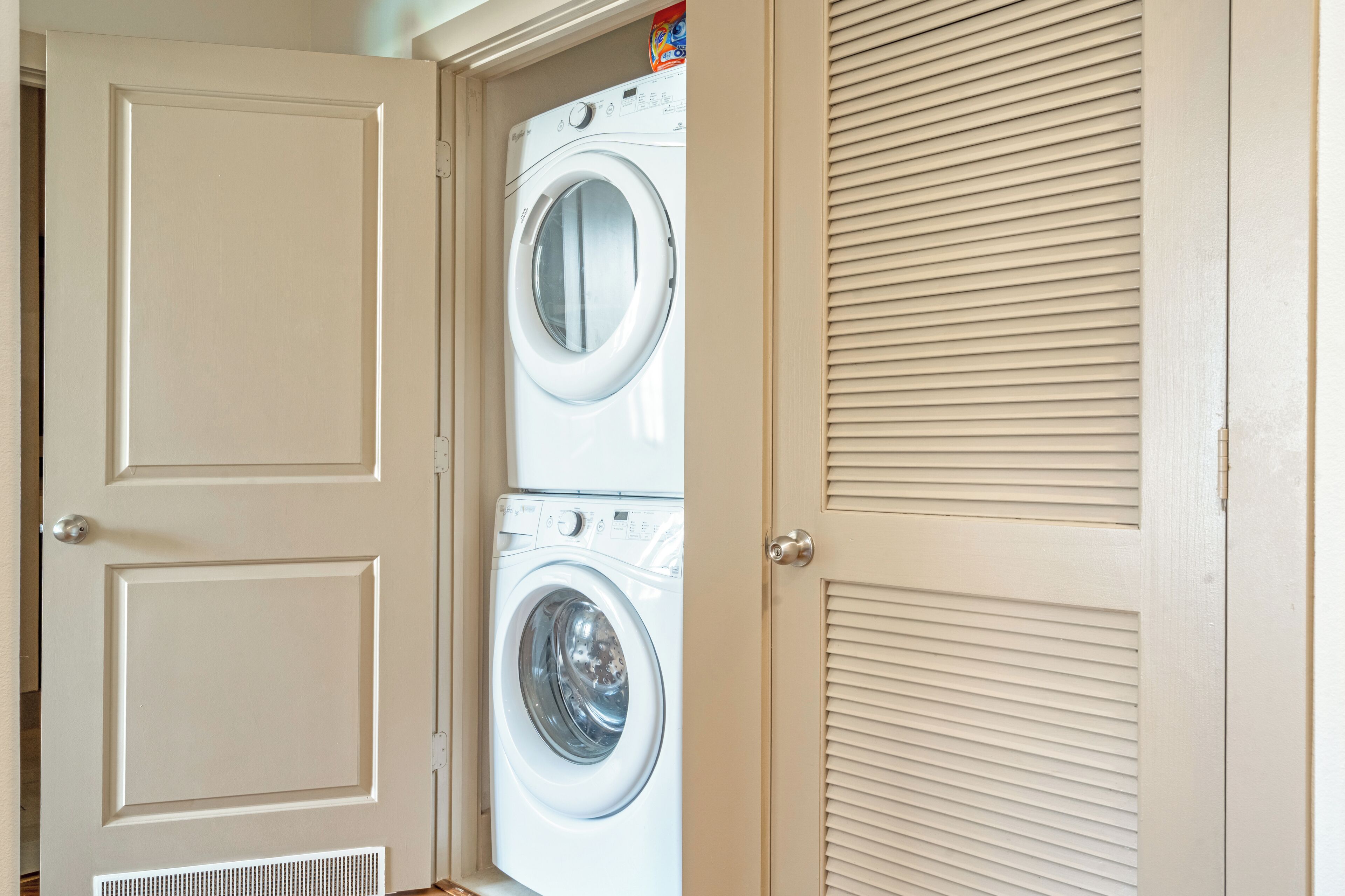 A laundry room with two stacked front-loading washing machines and a door with a vent.