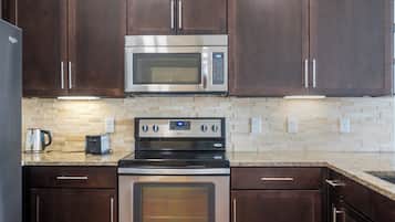 A kitchen with dark wooden cabinets, a stainless steel microwave, a built-in oven, a toaster, and a tiled backsplash.