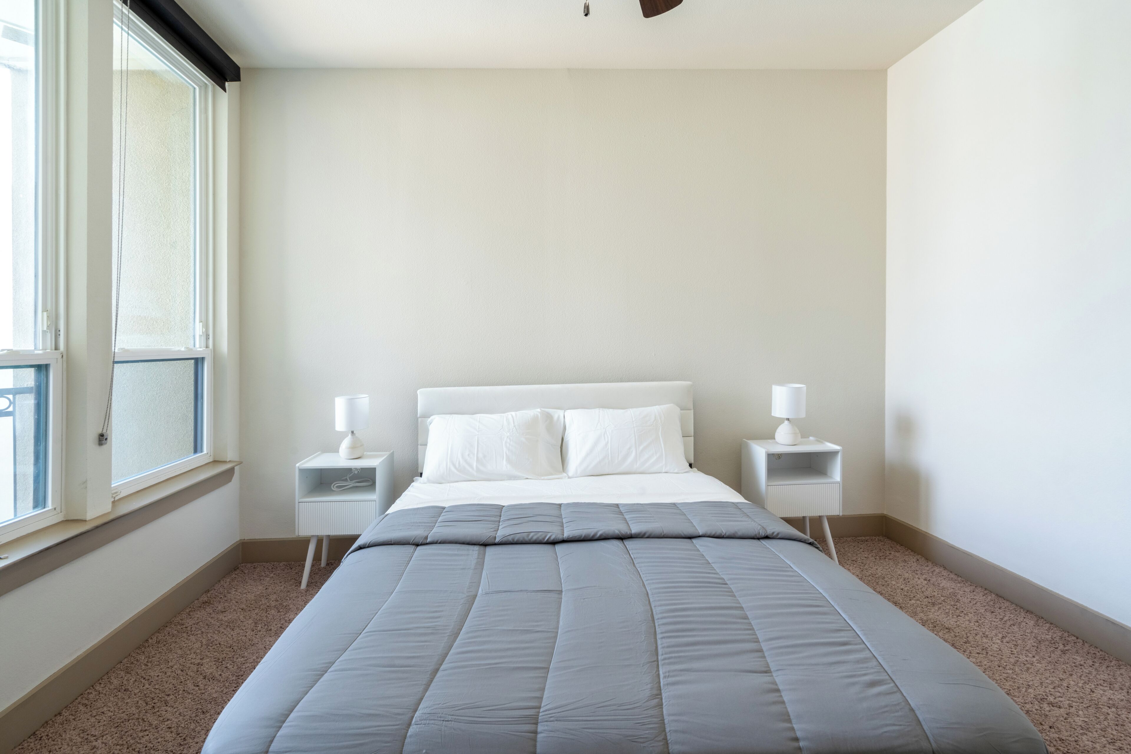 A bedroom with a bed, two bedside tables, a window, and a carpeted floor.