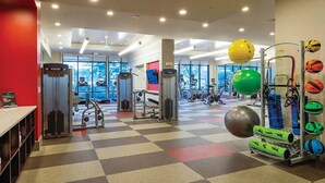 Et fitnesscenter med forskellig træningsudstyr, et skakternet gulv og store vinduer.