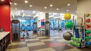 Uma academia com diversos equipamentos de exercício, piso xadrez e grandes janelas.
