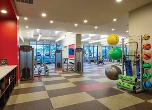 Ein Fitnessraum mit unterschiedlichen Trainingsgeräten, einem Schachbrettmuster-Boden und großen Fenstern.