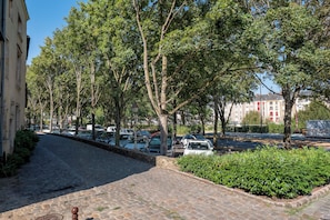 Eine von Bäumen gesäumte Kopfsteinpflasterstraße mit parkenden Autos.