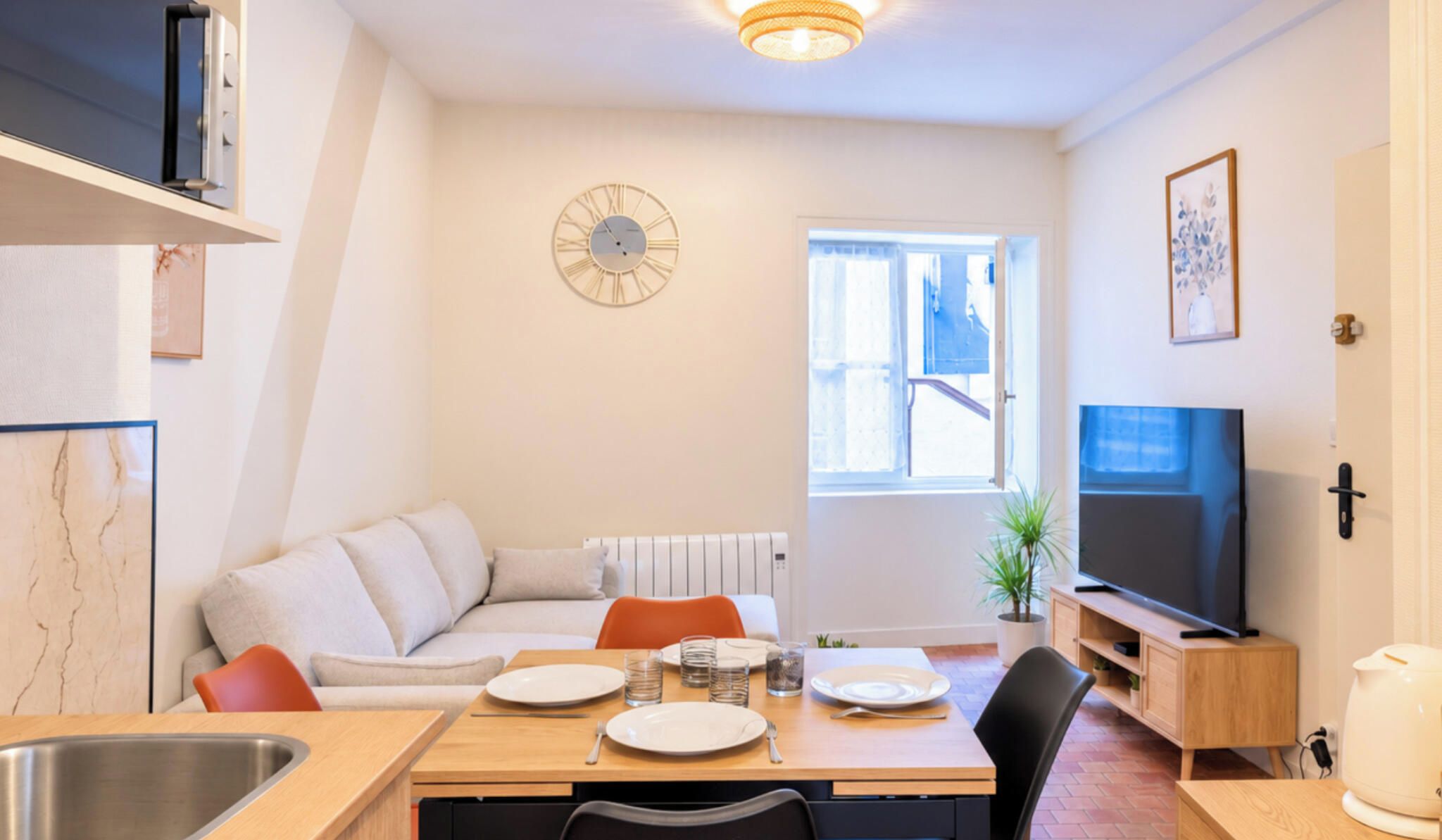 A modern living room with a dining area, a sofa, a TV, and a clock on the wall.