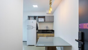 Cozinha compacta com geladeira, micro-ondas, cafeteira e mesa de vidro.