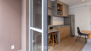 A modern kitchen with wooden cabinets, a stainless steel refrigerator, and a small dining area with a table and chairs. - Complete Studio 500m From the Subway Cpm1110 (São Paulo)