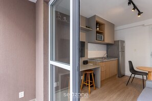A modern kitchen with wooden cabinets, a stainless steel refrigerator, and a small dining area with a table and chairs. - Complete Studio 500m From the Subway Cpm1110 (São Paulo)