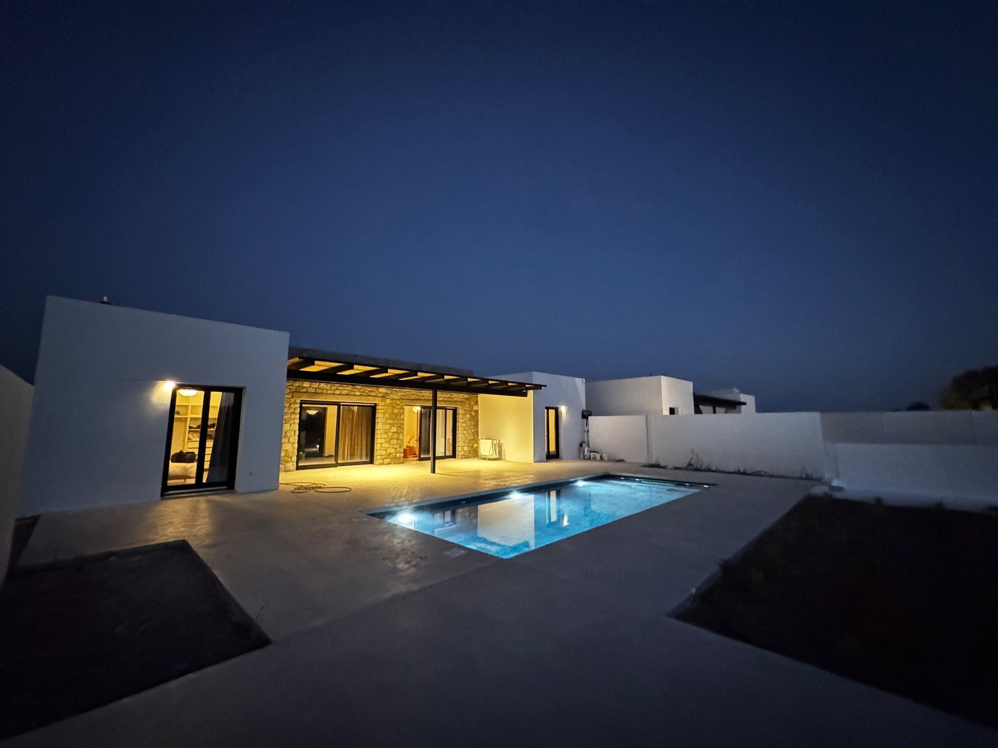 A modern house with a swimming pool, stone walls, and a covered patio area.