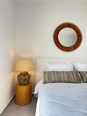 A bedroom with a bed, a round mirror, a bedside lamp, and a small wooden nightstand. - Mister X Private Villa with Pool & 3 Bedrooms in Naxos (Naxos)