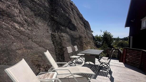 Terraza de madera con sillas de descanso y una mesa, con vistas a una ladera rocosa.