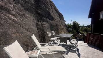 Une terrasse en bois avec des chaises longues et une table, offrant une vue sur une colline rocheuse.
