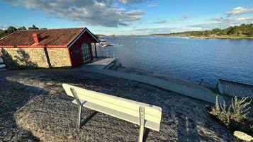 Une vue sur la côte, avec un bâtiment rouge portant l’inscription « SJOODEN » et un banc blanc sur une plage de galets.