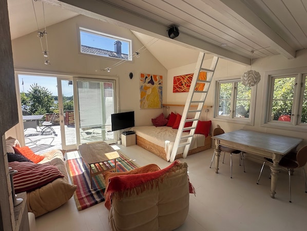 A room with a bed, a TV, a table, and a view of the outdoors.