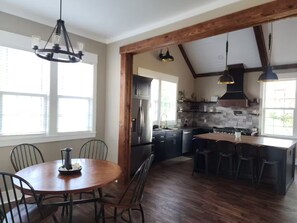 A spacious kitchen with a central island, wooden beams, and a dining area with a round table and chairs.