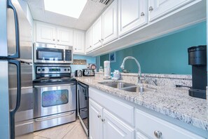 A modern kitchen with stainless steel appliances, white cabinetry, a granite countertop, and a teal backsplash. - Coastal Bliss and Beachfront Resort Oasis for 5! (Panama City Beach)